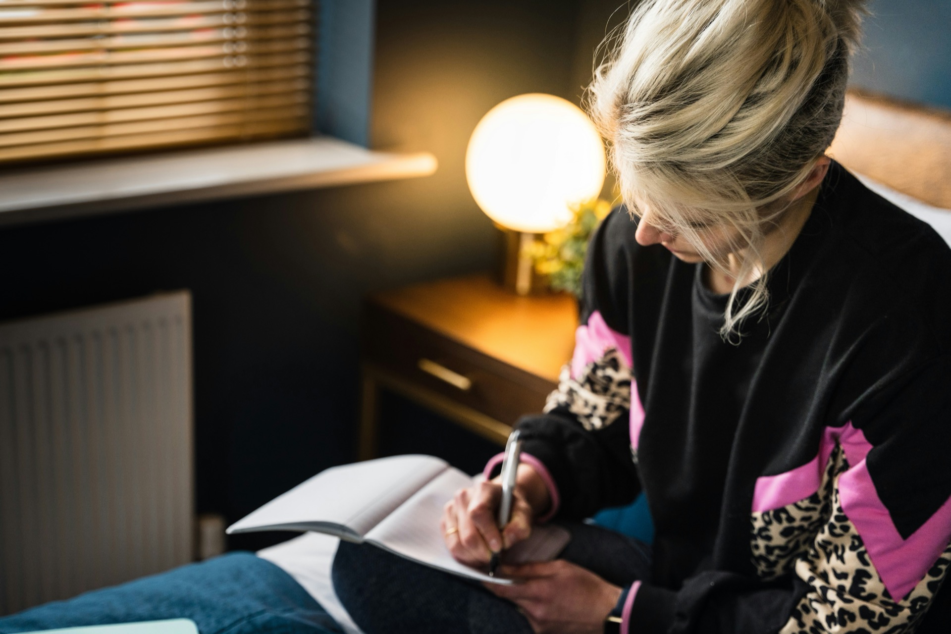 person writing in a notebook while seated indoors