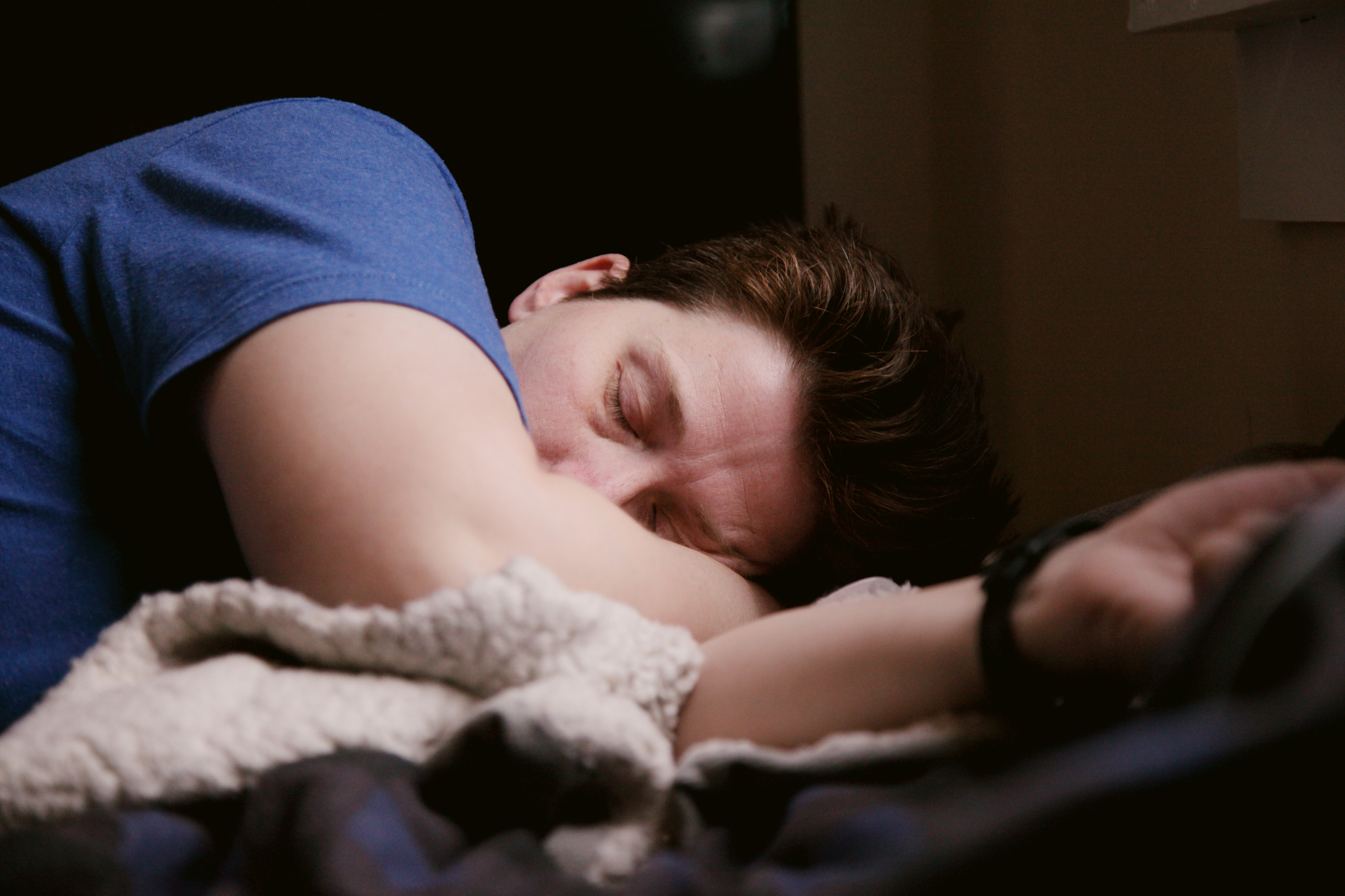 person sleeping on their side under a blanket in a dimly lit room