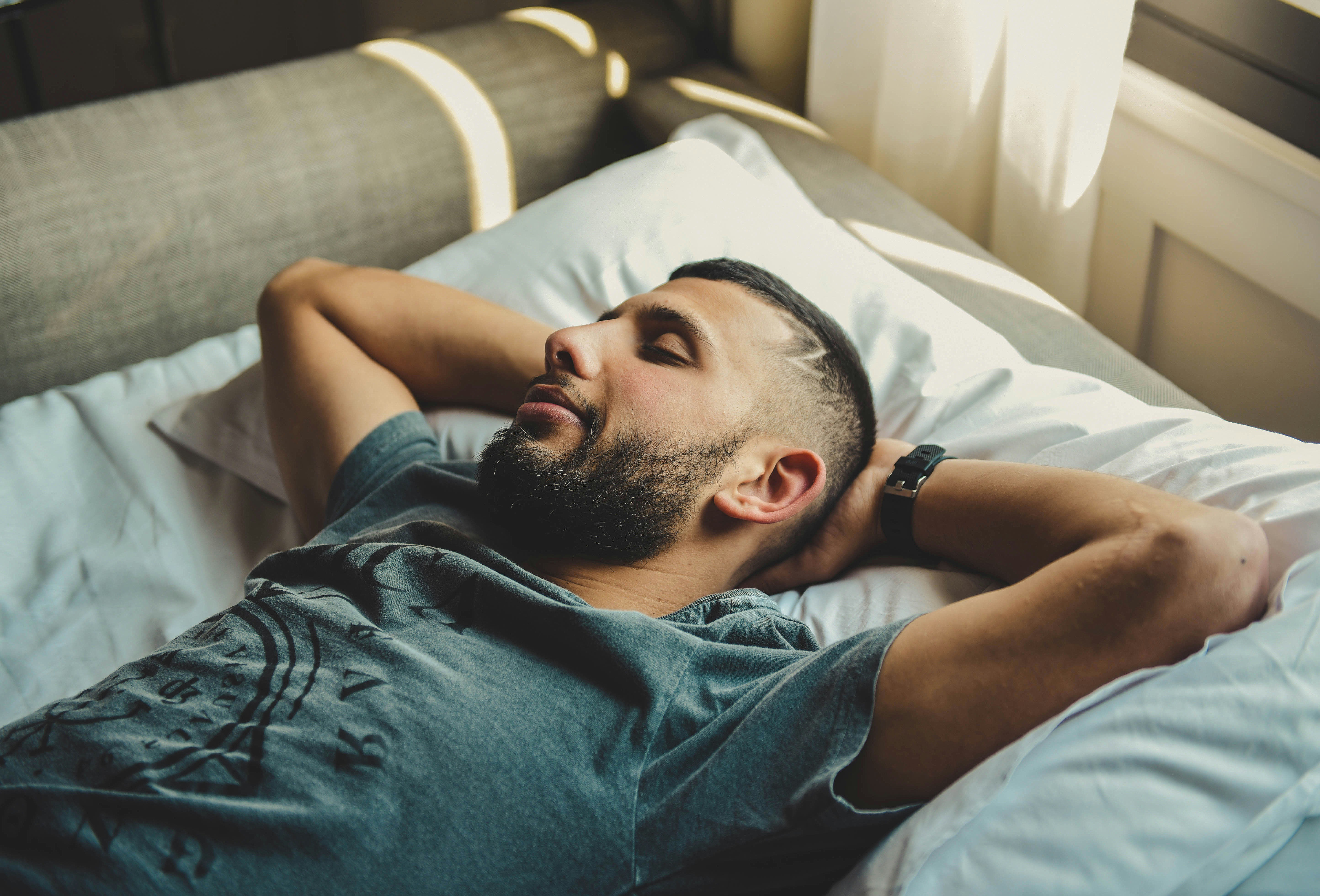 man resting in bed with eyes closed while wearing a wrist device