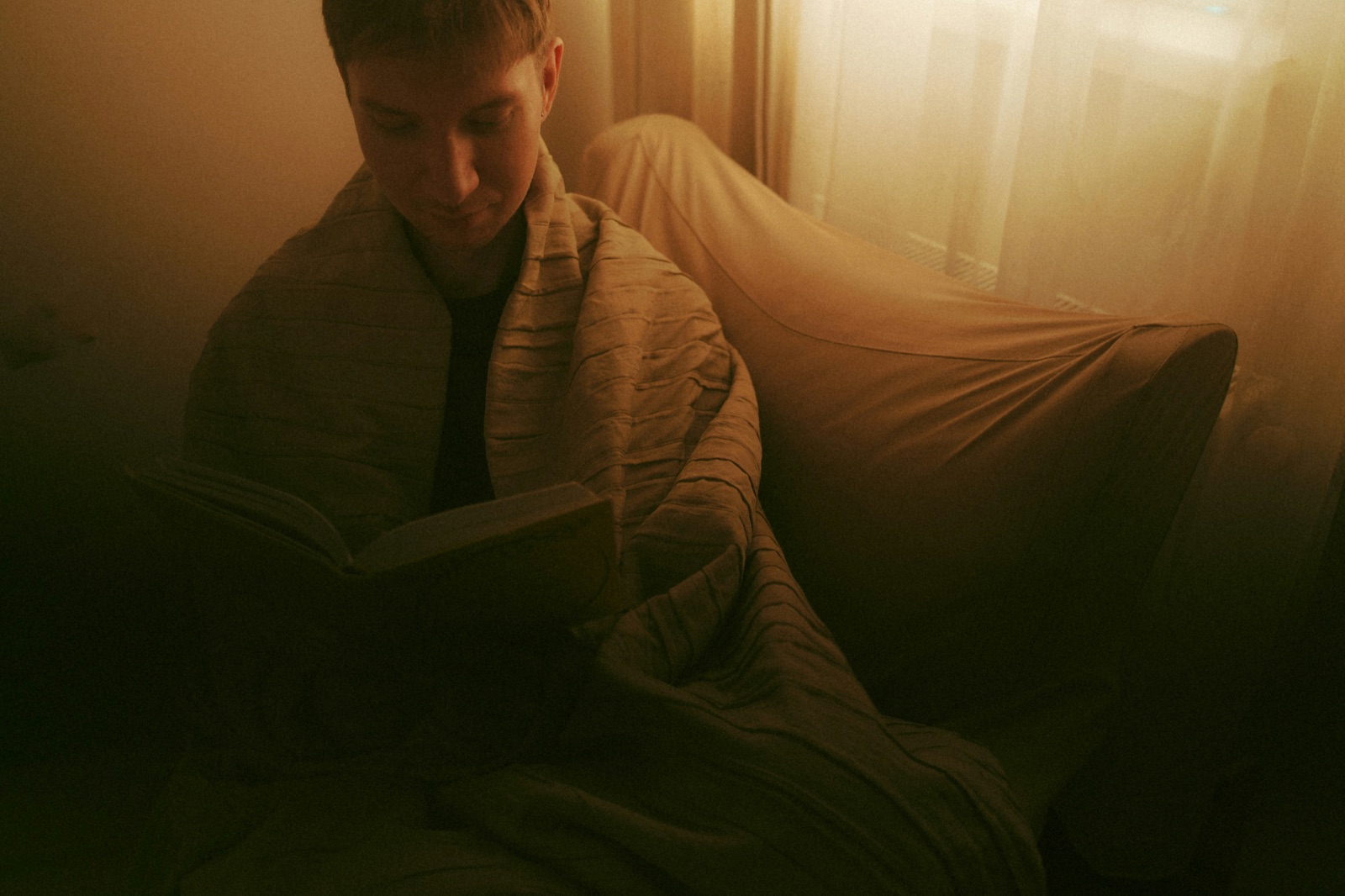 person wrapped in a blanket reading a book in warm evening light