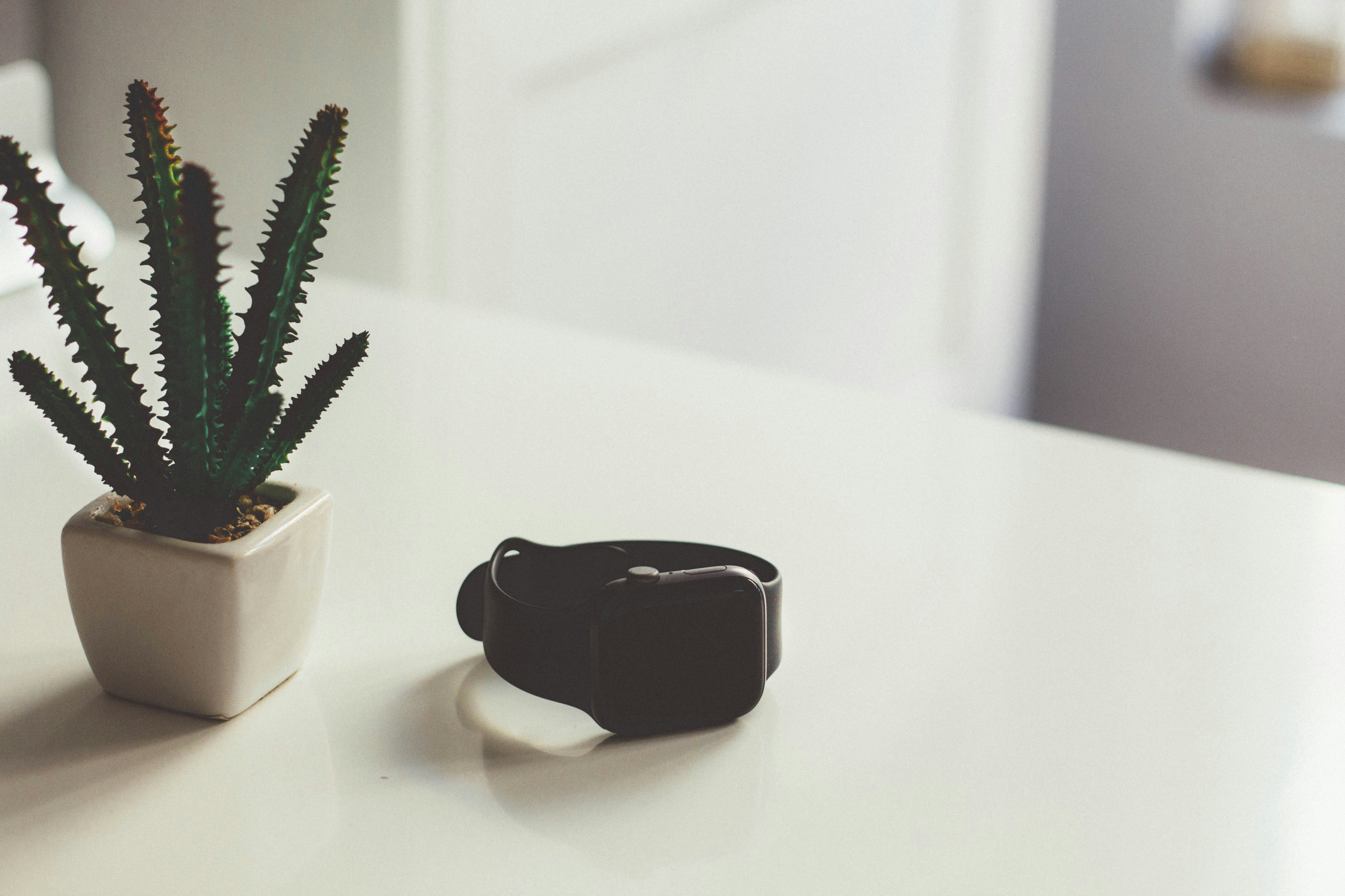 A smartwatch resting on a bedside table beside a small plant, representing everyday sleep tech and the gap between measuring sleep and improving it