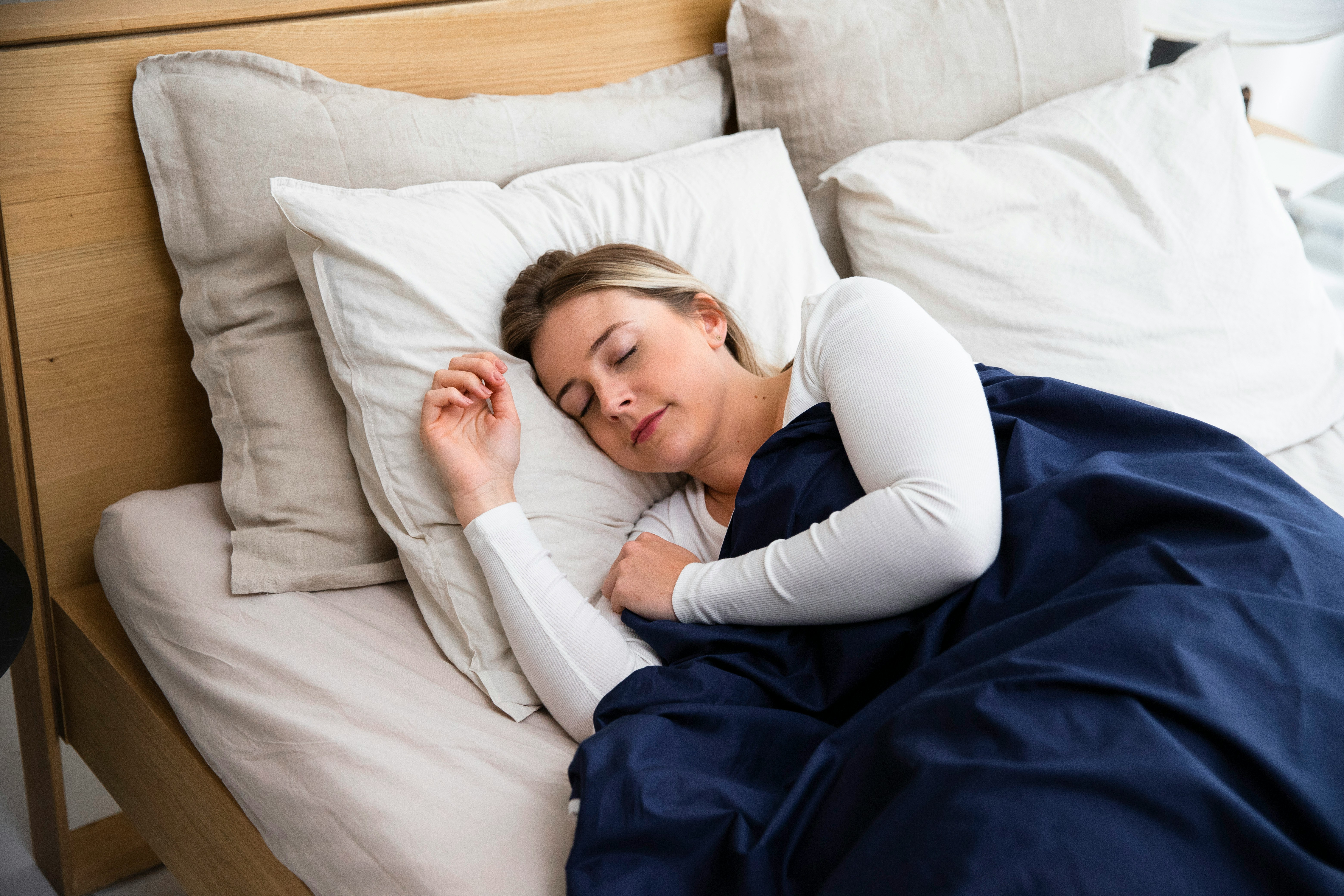 A calm, softly lit bedroom with clean white bedding representing the environmental conditions that support healthy sleep